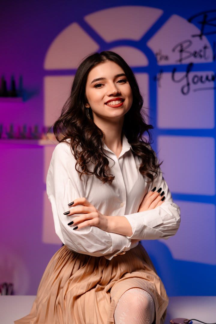 Maria zâmbind, cu brațele încrucișate și unghiile negre, în studioul ei, în tonuri calde